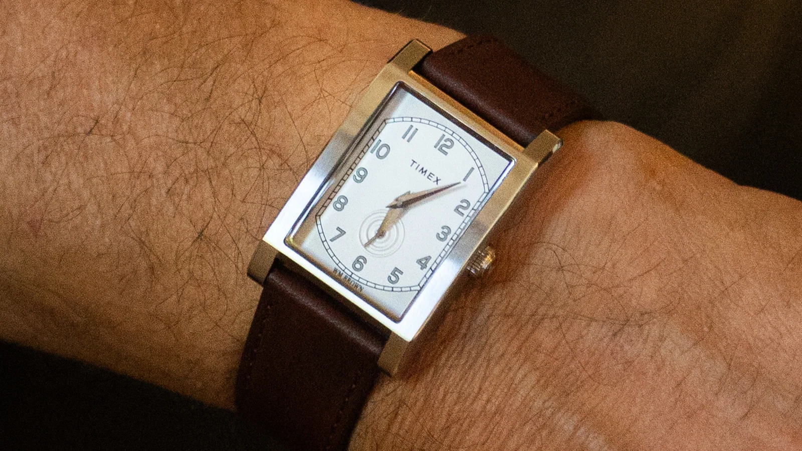 14341 TX TC 26 PFB desktop TWG069000 2 Ceas dreptunghiular WM Brown x Timex cu cadran alb, cifre arabe negre, subcadran pentru secunde mici și curea din piele maro pe un încheietura mâinii.
