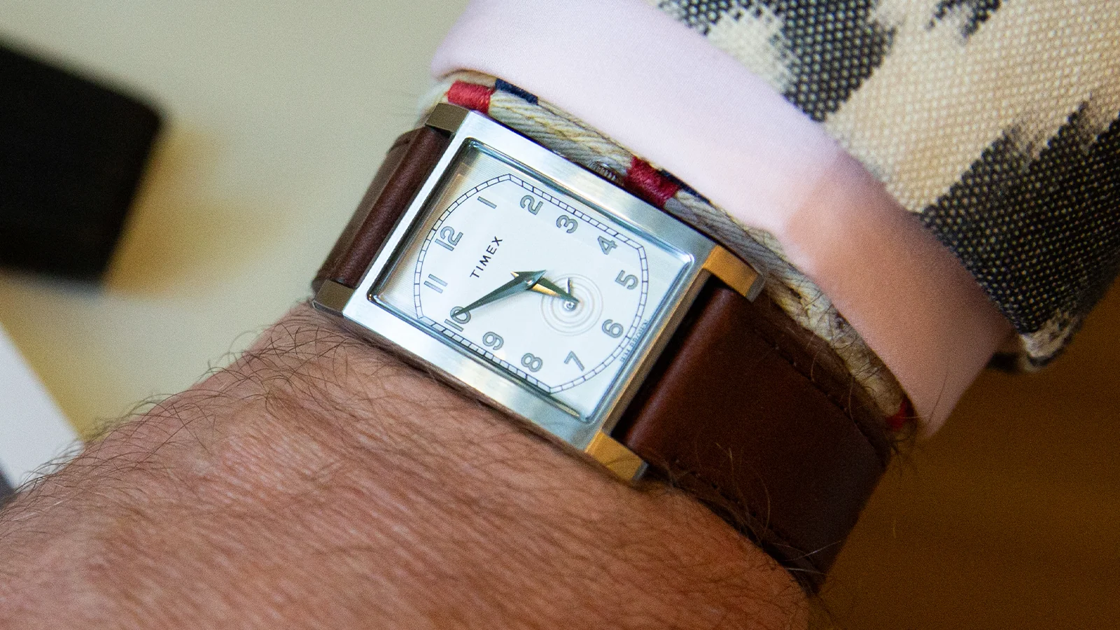 14341 TX TC 26 PFB desktop TWG069000 4 Ceas dreptunghiular WM Brown x Timex cu cadran alb și curea maro din piele, purtat peste mansetă roz și un sacou cu un model în alb-negru.