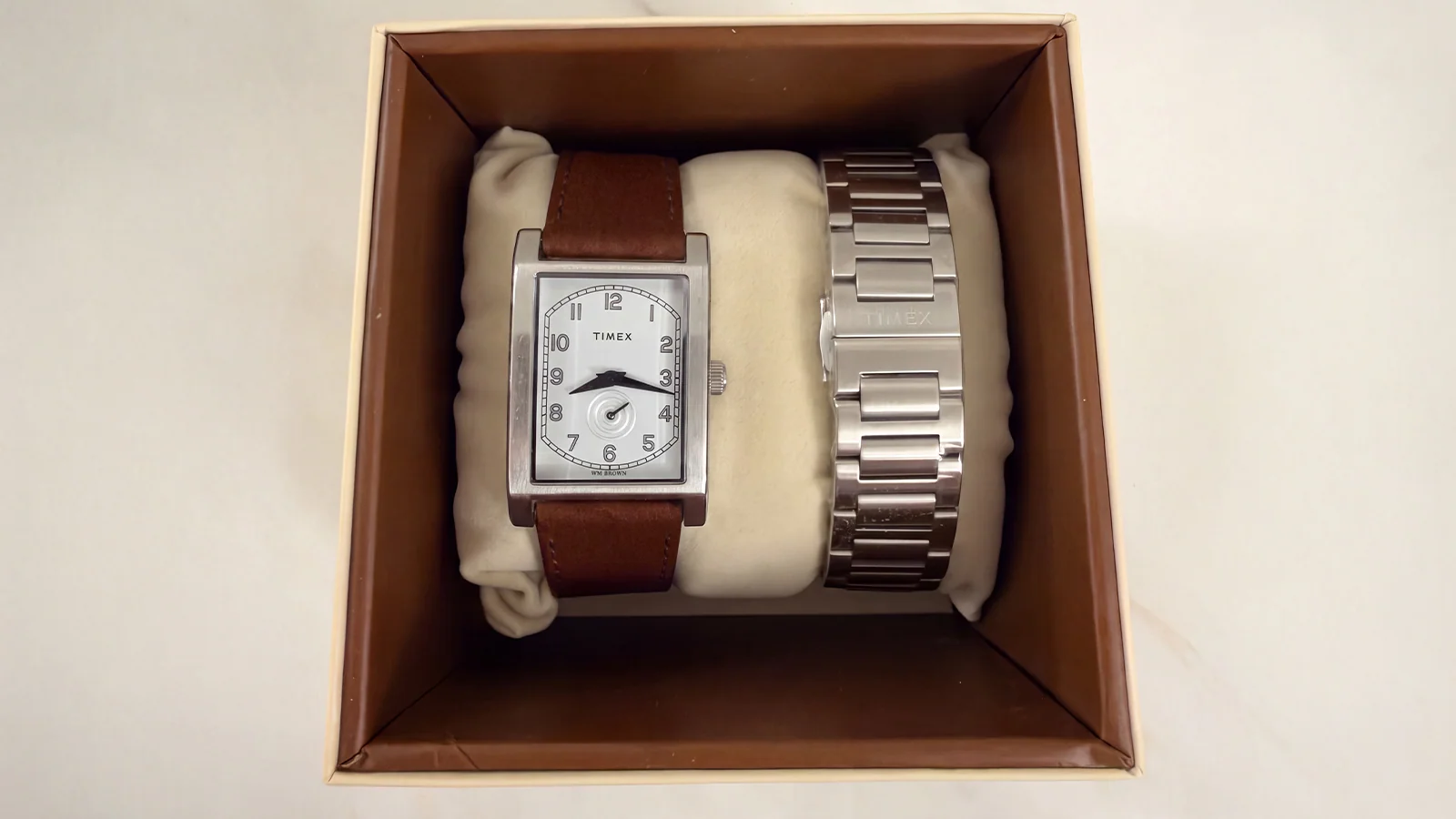 15341 TX TC 26 PFB desktop TWG069000 3 Ceas dreptunghiular Timex WM Brown cu curea maro din piele și o brățară metalică argintie într-o cutie de prezentare deschisă.