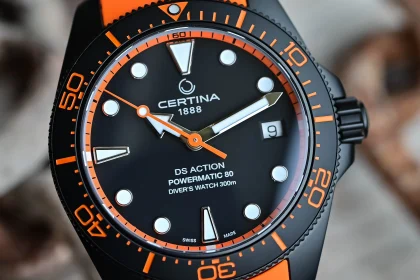 Ceas Certina DS Action Powermatic 80 cu cadran negru, marcaje și lunetă cu accente portocalii, curea portocalie din material sintetic.