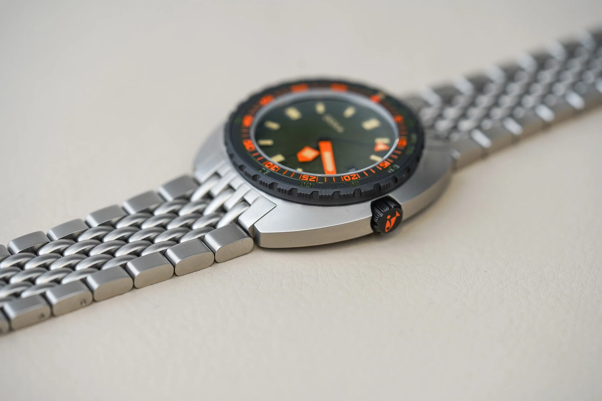 DSC02870 Ceas de scufundare cu brățară metalică, bezel negru cu marcaje portocalii, cadran verde închis și ace largi portocalii, coroană cu simbol portocaliu.