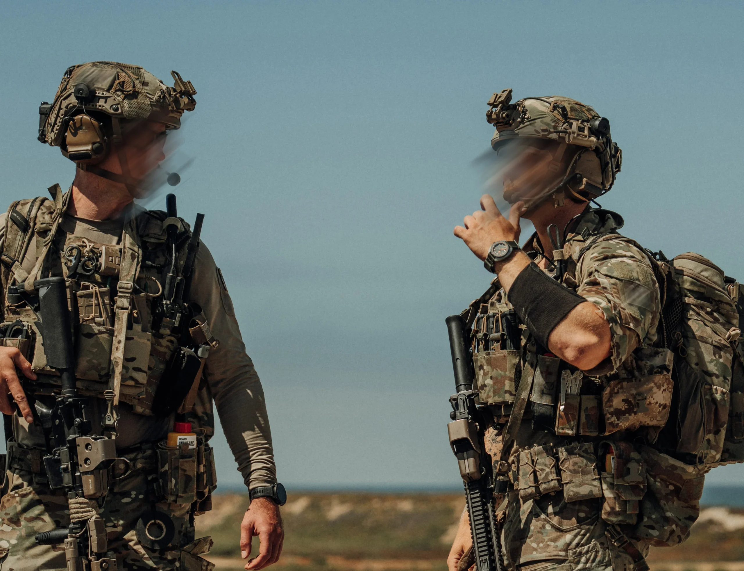 Frogger Navy Seal 5 scaled Doi soldați în echipament de luptă complet, purtând ceasuri negre la mâna stângă, într-un cadru outdoor sub cer senin.